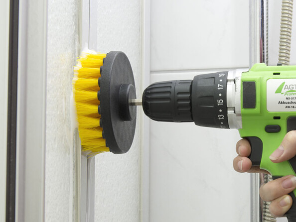 Visseuse verte et noire avec embout brosse ronde nettoyant une surface à la verticale