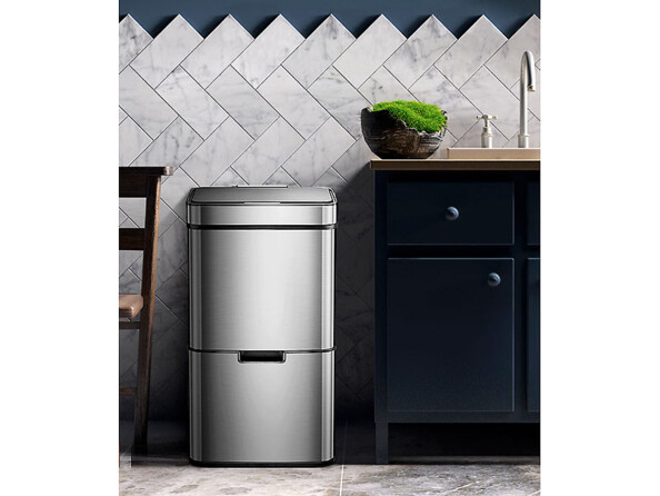 Mise en situation de la poubelle Infactory placée dans une cuisine entre un meuble avec robinet et une chaise