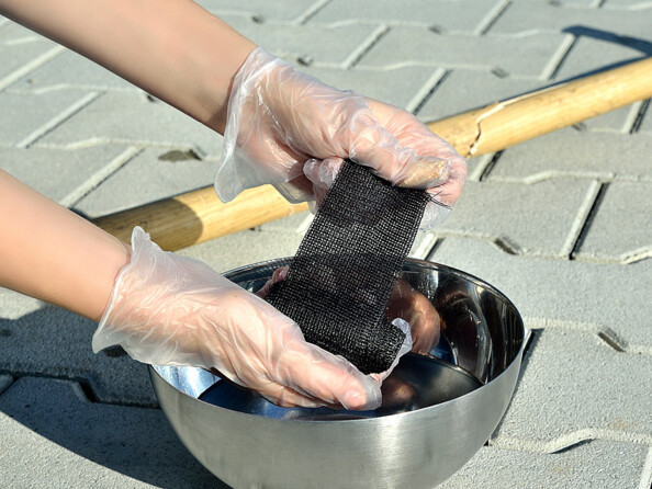 Humidification de la bande adhésive dans un bol en inox à deux mains protégées par des gants en plastique