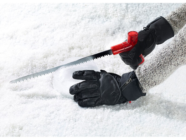 Deux mains avec moufles noires tranchant la glace avec la scie intégrée