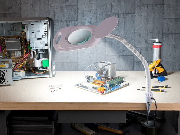 Mise en situation de la lampe-loupe fixée à un plan de travail d'atelier avec matériel informatique éclairé en cours de réparation