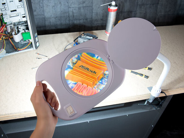 Main maintenant la poignée de la lampe-loupe au-dessus d'un composant électronique ASRock sur une surface de travail dans un atelier de bricolage