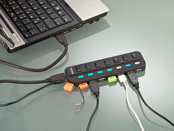 Mise en situation du hub Xystec branché à un ordinateur portable par câble Mini-USB et à un adaptateur secteur avec clé USB, dongle de souris et 3 câbles d'alimentation et de transfert de divers appareils mobiles branchés à 5 des 7 ports USB du hub