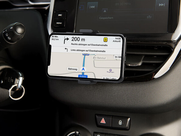 Mise en situation d'un support smartphone maintenant entre ses deux pattes un smartphone allumé sur une application de navigation GPS et fixé à une grille d'aération du tableau de bord central d'un véhicule en marche