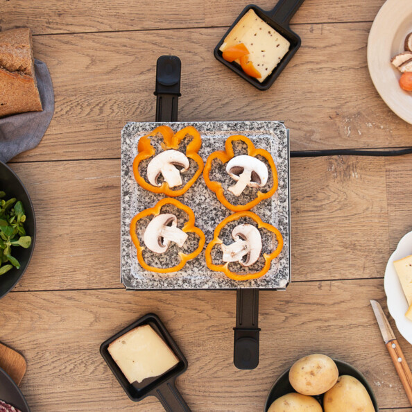 Des champignons et des poivrons en train de griller sur le plateau en granit de l'appareil à raclette Livoo.