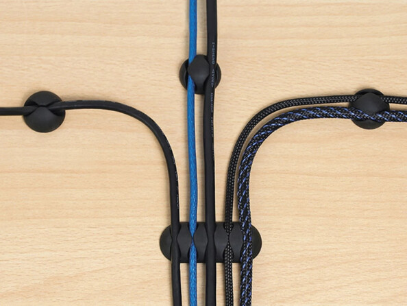 Vue du dessus de 4 organiseurs de câble différents guidant 5 câbles vers devant, à droite et à gauche d'une plateforme aspect bois pour ranger les câbles et éviter les emmêlements