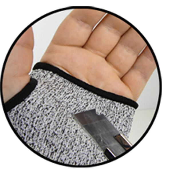 Test de l'efficacité d'une manchette anti-coupure Genius Ideas en tissu coloris gris à travers un tentative de coupe au cutter sur la paume de la main gauche protégée par le gant résistant