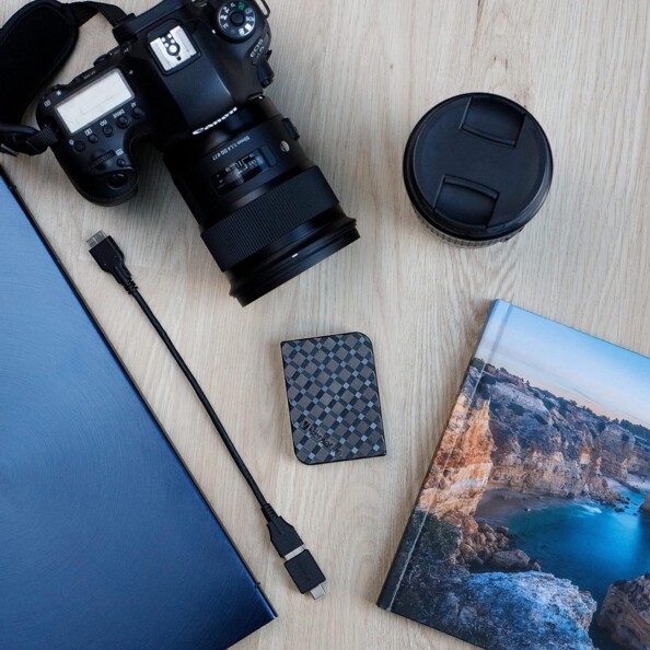 Disque dur externe SSD Verbatim 1 To posé à côté d'un câble et d'un adaptateur USB posés à côté de livres et d'un appareil photo au cache retiré