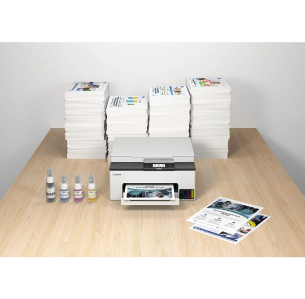 Imprimante, copieur et scanner 3 en 1 posé sur une table de bureau en bois clair à côté de plusieurs piles de documents imprimés et de quatre bouteilles d'encre de recharge (1 x cyan, 1 x magenta, 1 x jaune, 1 x noir)