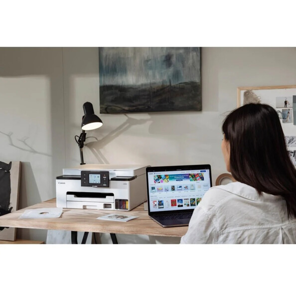 Femme assise à un bureau devant un ordinateur portable réalisant des impressions par le biais de l'imprimante Canon Maxify GX1050