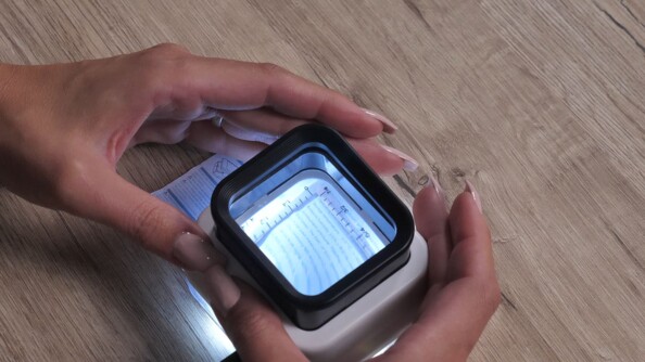 Mise en situation de l'éclairage LED blanc et de la règle graduée de la loupe posée sur un document et tenue à deux mains