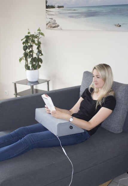 Vue plongeante sur une femme couchée sur un canapé avec les mains posées sur le coussin chauffant et massant branché à l'alimentation