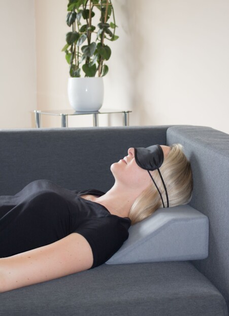 Photo portrait d'un buste d'une femme avec la nuque posée sur l'oreiller trapézoïdal Hydas sur un canapé et portant un masque de nuit noir pendant sa sieste