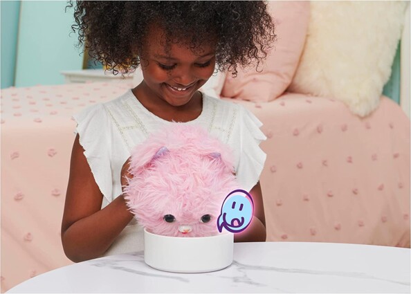 Petite fille noire en robe blanche faisant semblant de faire manger la peluche chaton dans une gamelle blanche sur une table en marbre avec logo exprimant la faim