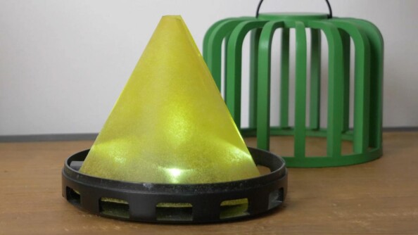 Pyramide jaune illuminée par 4 LED blanches sur le socle doté d'ouvertures latérales coloris noir à côté de la cage verte auparavant posée sur le dessus