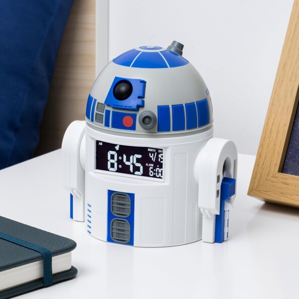 Horloge et réveille-matin R2D2 Star Wars posé sur une table de nuit moderne blanche à côté d'un tableau en ardoise et d'un calepin fermé