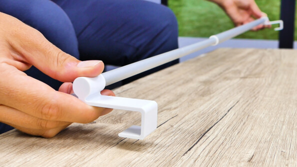 Personne à genou tenant dans ses mains la barre télescopique de la tringle à rideaux grise et blanche avec crochets