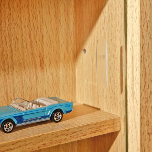 Zoom sur les trous situés le long de la paroi gauche de la vitrine pour réglage de la hauteur des étagères, avec modèle réduit d'une voiture ancienne posée sur l'une d'elles