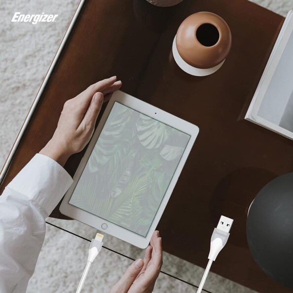 Mise en situation du câble Lightning en cours de branchement à un iPad posé sur un bureau par une personne le tenant par les coins