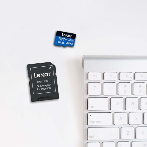 Carte MicroSDXC Lexar avec adaptateur SD posés côté face sur leur puce à côté d'un clavier blanc sans fil