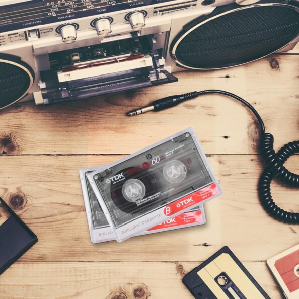 Deux cassettes audio posées devant une radio à côté d'un câble jack et d'autres cassettes sur une table en bois