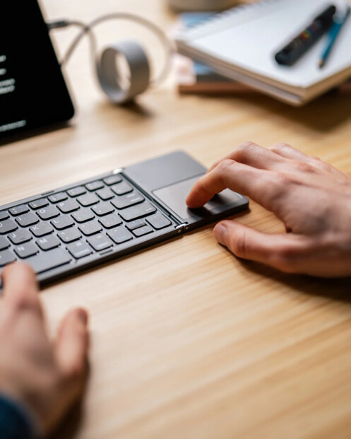 Gros plan sur l'utilisation du mini pavé tactile intégré au clavier pliable AZERTY sur un bureau en bois