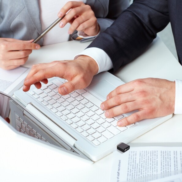 Mise en situation du dongle wifi 6 Archer TX1800U AX1800 branché au port USB-A d'un PC portable sur lequel un homme en chemise fait une présentation à une collègue en costard elle aussi