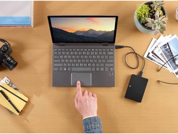 Utilisation du disque dur externe Seagate Expansion branché au port USB d'un PC portable sur lequel une personne travail sur un bureau à côté d'objets divers et variés