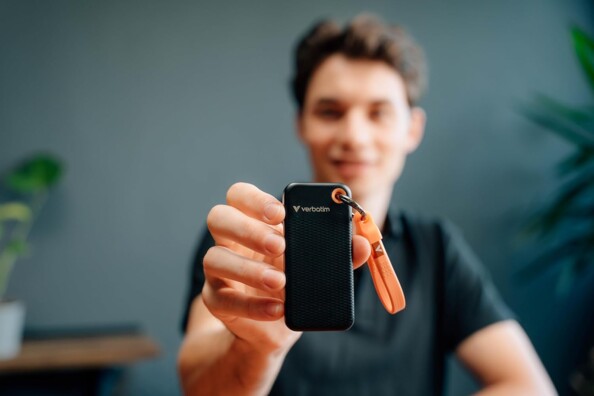 Jeune homme souriant main droite tendue montrant le disque SSD de poche Verbatim