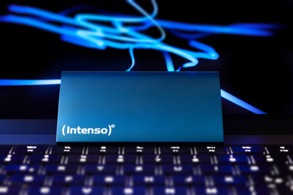 Mise en situation du disque externe SSD bleu posé contre l'écran d'un PC portable ouvert devant un clavier de la même couleur