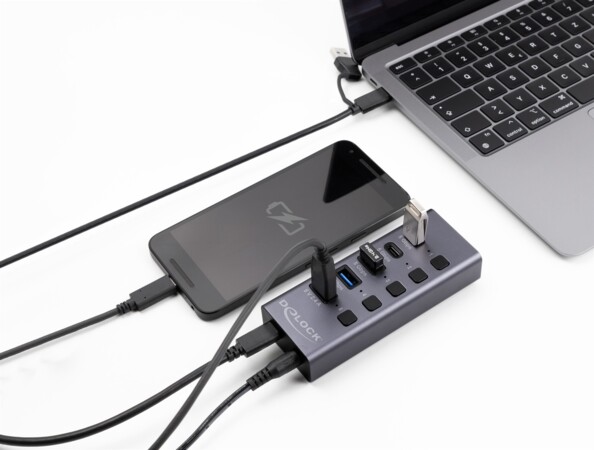 Mise en situation de la station d'accueil USB branchée à un PC portable éteint, à un smartphone en cours de chargement et à diverses clés USB type C ou A