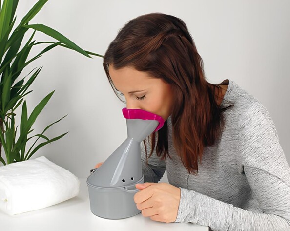 Femme inhalant par le nez et la bouche le contenu de l'inhalateur avec les deux mains sur les poignées de l'appareil