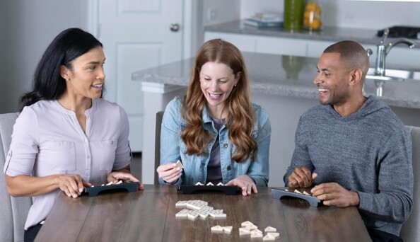 Trois joueurs souriant autour d'une partie de Triominos Classic dans un intérieur moderne