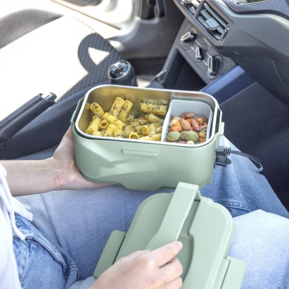 Mise en situation de la boîte repas en plastique et inox coloris vert dans une voiture sur les genoux d'une personne