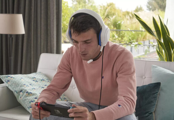 Adolescent en pull saumon assis sur le canapé et concentré sur sa partie de jeu vidéo sur Nintendo Switch branchée au casque audio The G-Lab
