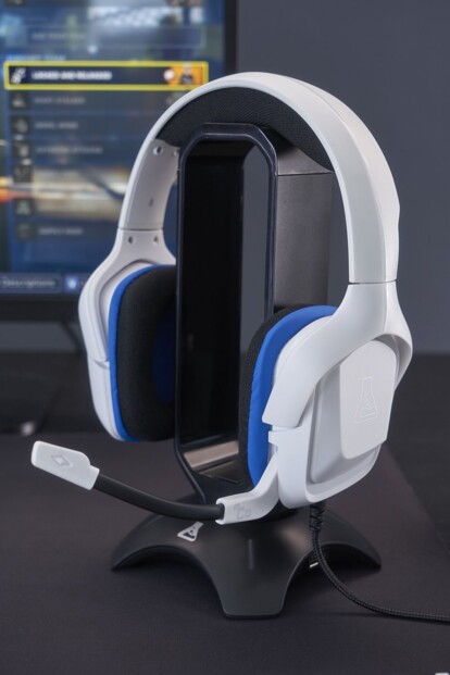 Micro-casque filaire Korp Cobalt coloris blanc pour gamer posé sur support sur un bureau à côté d'un PC gaming