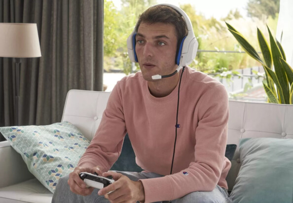 Jeune homme jouant en immersion à un jeu vidéo assis le canapé d'un salon avec manette en main et micro-casque Korp Cobalt sur les oreilles
