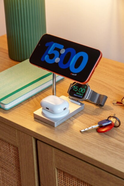 Mise en situation du chargement d'un smartphone à l'horizontale, d'écouteurs sans fil dans leur boîtier et d'une montre connectée sur les trois surfaces de charge à induction Qi compatibles MagSafe magnétiques de la station posée sur un meuble en bois