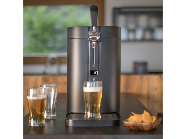 Mise en situation de la tireuse à bière Livoo DOM511 moderne coloris noir sur un plan de travail d'une cuisine avec ramequin remplit d'apéritifs et service de 3 verres à bière remplis dont 1 sur le plateau égouttoir de la tireuse