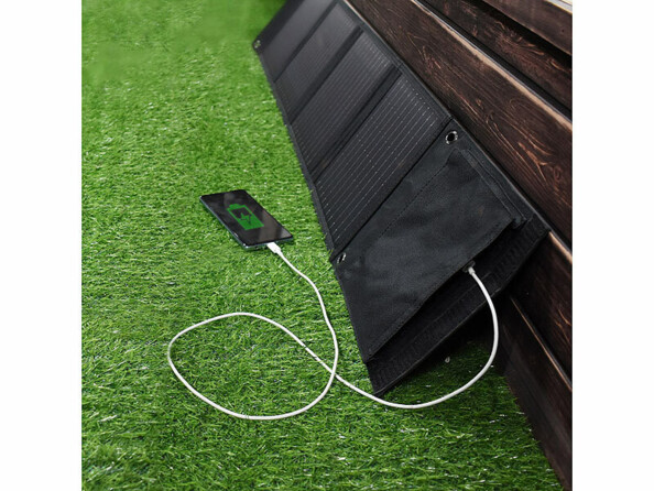 Smartphone et panneau solaire posés sur du gazon synthétique contre une barrière en bois avec smartphone en cours de chargement par le biais du chargeur intégré au module solaire