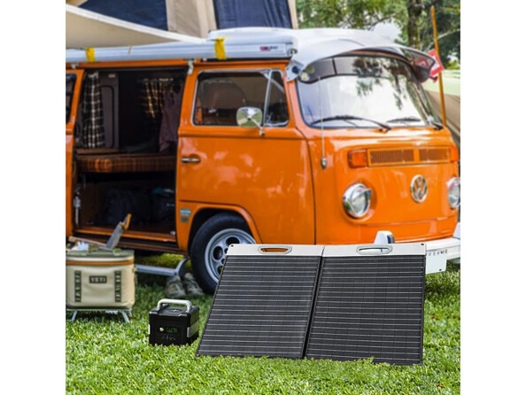 Van orange ancien avec porte latéral ouverte et toile de protection tendue, garé à côté du générateur solaire HSG-650 et du panneau solaire Revolt 100 W raccordés