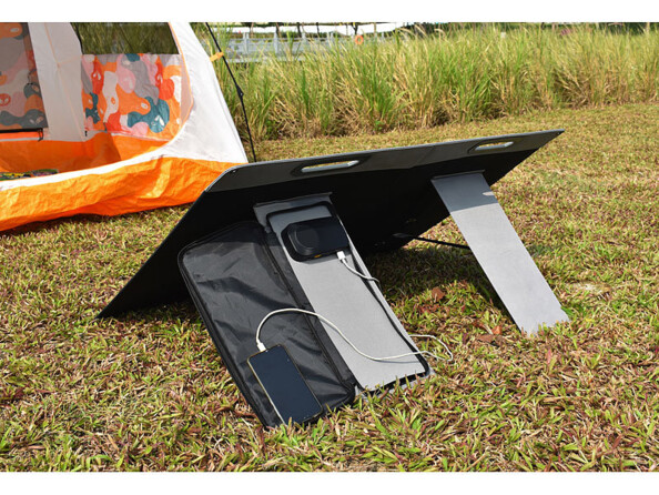 Panneau solaire 100 W déplié sur du gazon en camping et tenant incliné grâce à ses pieds de support, avec régulateur de charge apparent