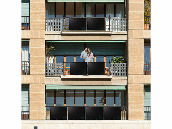 Panneaux solaires installés sur plusieurs balcons d'un immeuble dont l'un où se trouve une famille de trois personnes