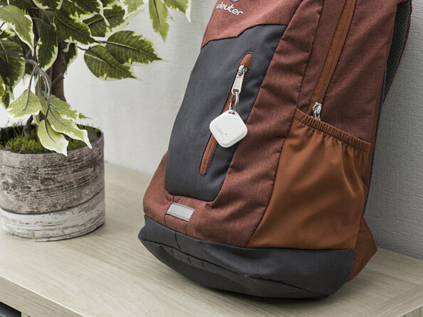 Localisateur d'objet attaché à une tirette d'un sac à dos posé sur un meuble à côté d'une plante en pot