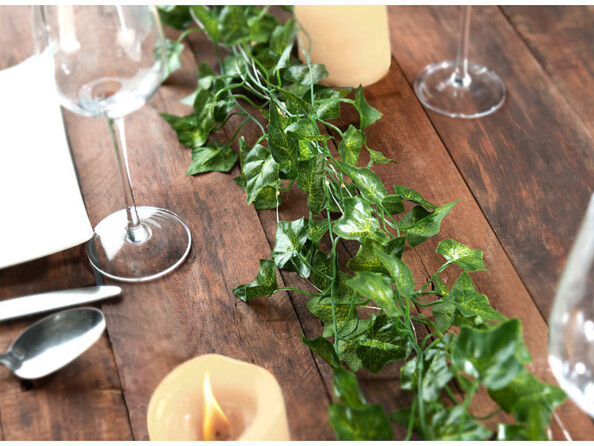 Mise en situation de guirlandes de lierre décorant une table à manger sur laquelle des couverts et des bougies sont posés