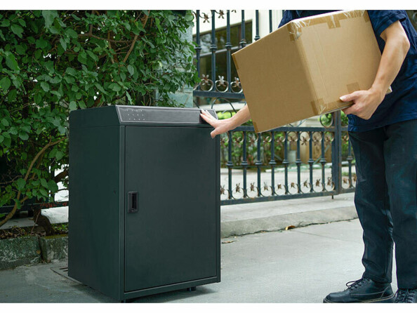 Facteur avec colis dans les bras ouvrant la boîte aux lettres connectée pour livraison avec empreinte digitale