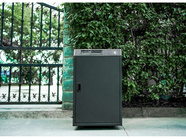 Boîte pour lettres et colis placée sur un sol pavé à côté d'un portail en métal menant à une propriété