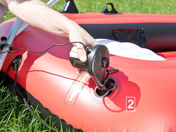 Mise en situation d'une personne entrain de gonfler un bateau pneumatique rouge et noir avec le gonfleur électrique Pearl en extérieur avec les rames du bateau posées dessus