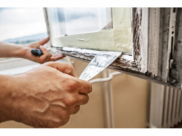 Application du mastic en fibre de verre sur le bord d'une fenêtre en bois délabrée en intérieur à l'aide d'une spatule tenue dans la main d'un homme tenant de l'autre main le carreau