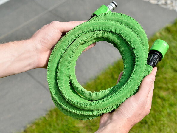 Deux mains tenant le tuyau d'arrosage extensible coloris vert enroulé sur lui-même